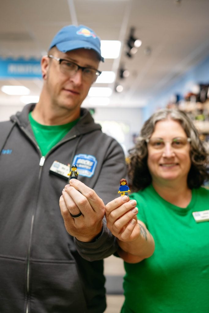 Anne and Demetrius display two of their custom LEGO minifigure creations, holding them up for the camera.