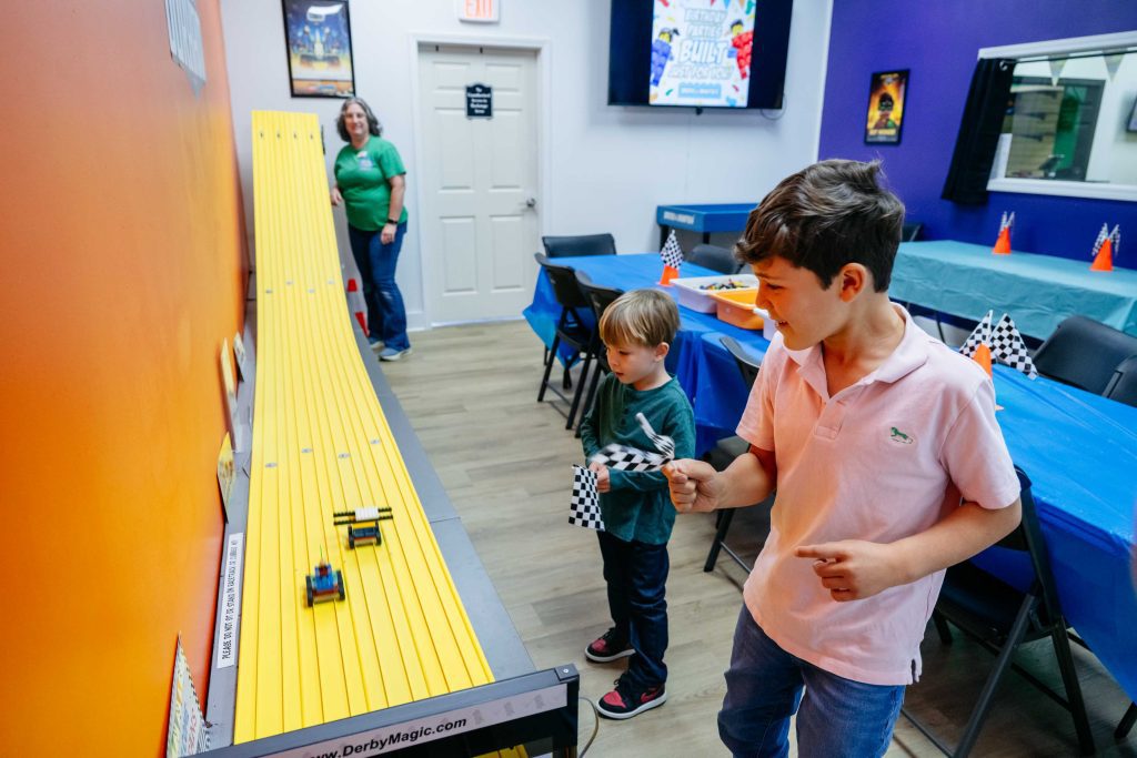 Isaac and Lennox cheer as Anne releases their LEGO cars, sending them racing down the Bricks & Minifigs Durham track.