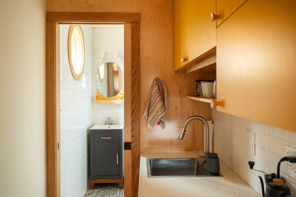 Galley kitchenette with yellow cabinets and a sink leading to a tiled bathroom with a round window.