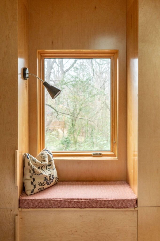 Cozy window seat built into a loft with wood paneling, a cushion and a view of trees outside.