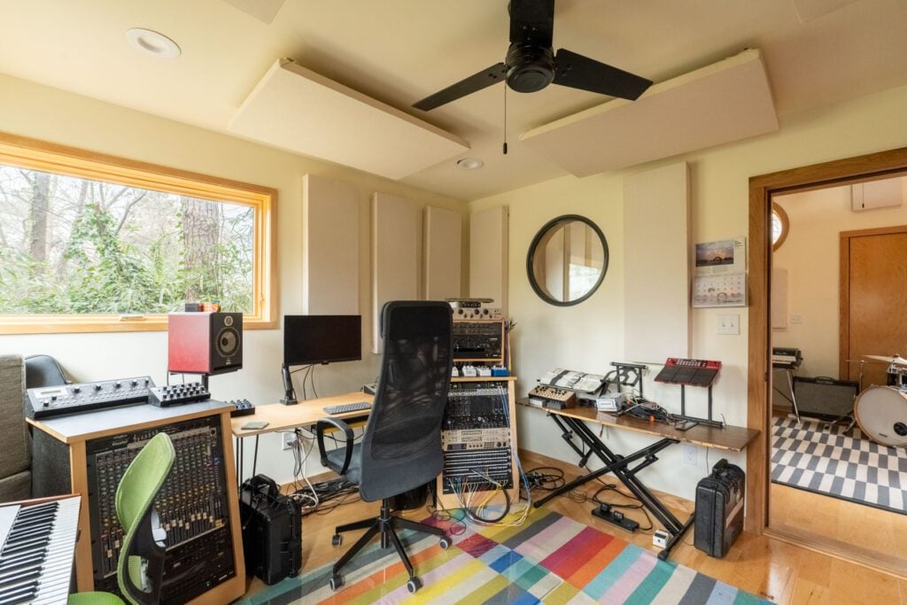 Control room in the recording studio with mixing equipment, acoustic panels and a window overlooking trees.