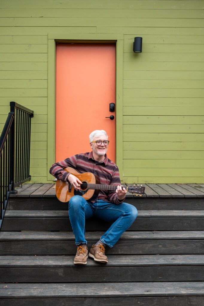 James sitting outside on steps playing an acoustic guitar.
