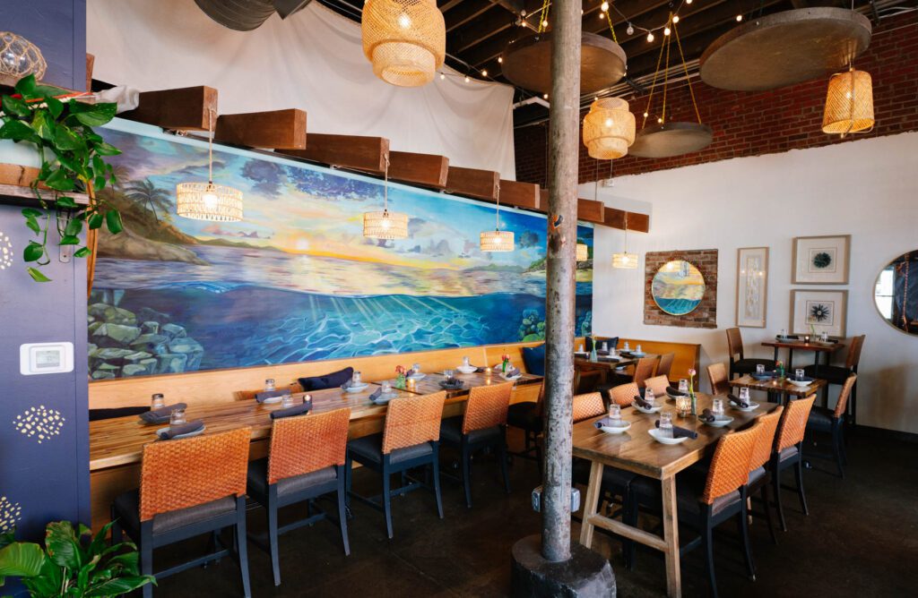 Dining room at Nerra with an ocean mural featuring waves, palm trees and a sunset.