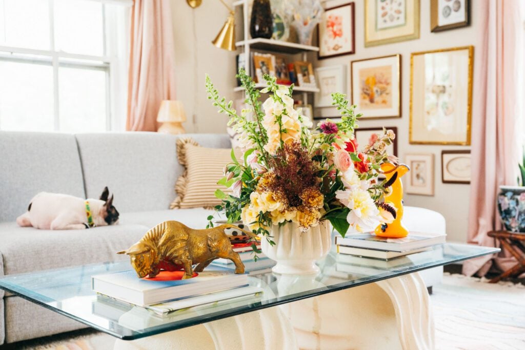 Colorful living room with floral arrangement, coffee table books and decorative accents styled on a glass coffee table in Courtney Hayes’ home.