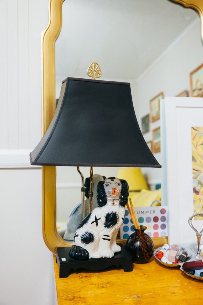 Black-and-white porcelain dog vase on a wooden side table in front of a gold-framed mirror.