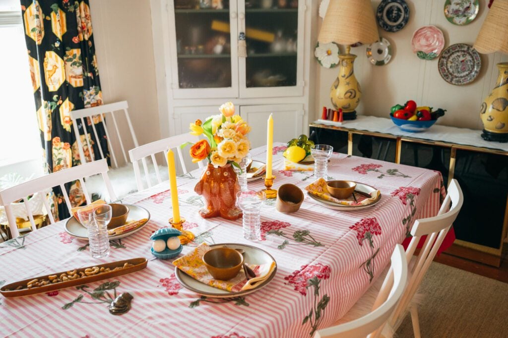 Dining table with a pink floral tablecloth, stacked plates, candles and colorful vintage-inspired décor in a cozy dining room.