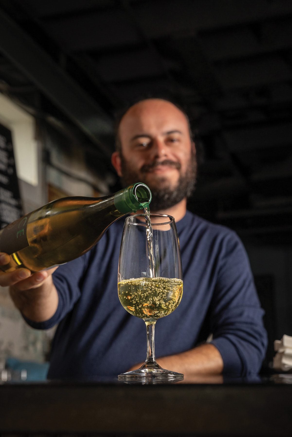 Delia owner Jesse Gerstl pours white wine into a glass at the bar.