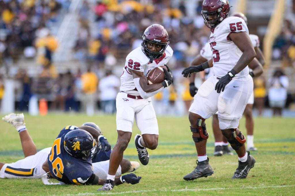 NCCU football player wearing No. 22 runs with the ball as two A&T players fall to the ground behind him during the homecoming game.